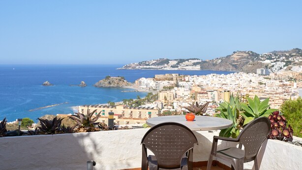 Terraza con dos sillas y una mesa con vistas a una ciudad costera.