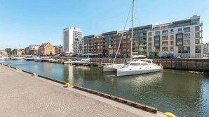 Eine Marina mit vertäuten Booten, eine Uferpromenade und moderne Gebäude im Hintergrund.