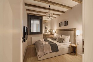 A bedroom with a bed, bedside tables, a window with blinds, a radiator, and a chandelier. - Granaria C105 | Best Location (Gdańsk)