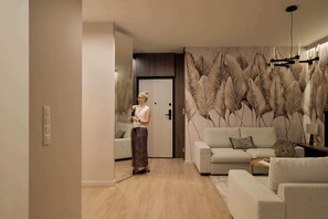 A modern living room with a sofa, a coffee table, and a decorative leaf-patterned wall. - Granaria C105 | Best Location (Gdańsk)