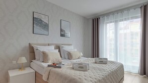 A bedroom with a bed, nightstand, lamp, and two framed pictures on the wall. - Waterlane SPA E7 | Spa, Pool & Gym | Riverside (Gdańsk)