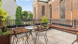 En terrasse med et bord og stole, en murstensbygning med buede vinduer og et gelænder af metal.