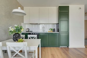 Une cuisine moderne avec des meubles blancs, une table à manger avec des chaises et un luminaire suspendu.