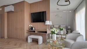 Uma sala de estar moderna com televisão de tela plana, armários de madeira, um banco, mesa de centro de vidro e um sofá.