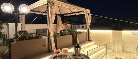 A rooftop terrace with a glass table, a pergola, and outdoor seating.