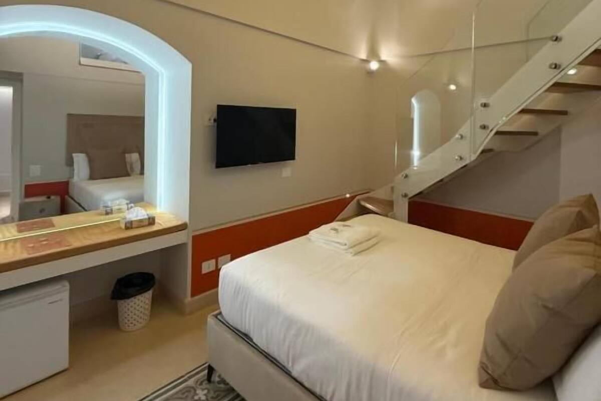 A bedroom with a bed, a mirror, a TV, and a staircase.