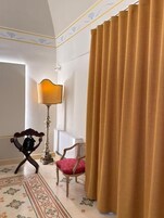 Una stanza con una moquette decorata, una sedia con un cuscino rosso, una lampada e un lampadario da terra.
