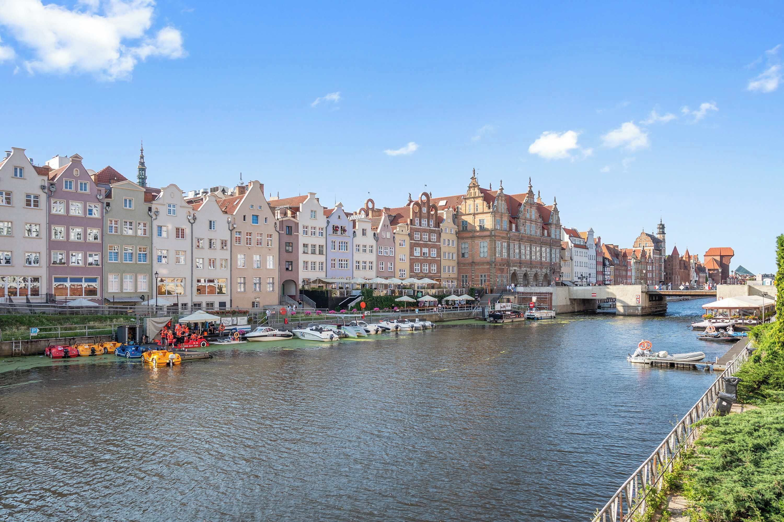 Une rivière où l’on peut voir des bateaux, un pont et des bâtiments aux couleurs vives le long de la rive.