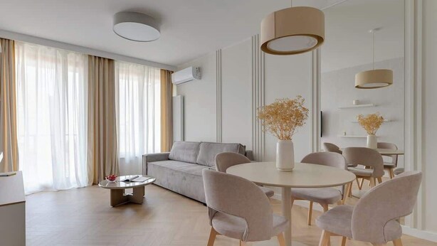 Ein modernes Wohnzimmer mit einer Couch, einem runden Esstisch und Stühlen. Über dem Tisch befinden sich Pendelleuchten.