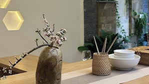 A wooden reception desk with a stone vase containing a branch with flowers, a woven basket with chopsticks, and a glass of water. - Bliss Home (Da Nang)