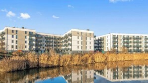 Een modern appartementencomplex met meerdere balkons, een reflecterend waterlichaam op de voorgrond en een heldere lucht.