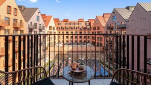 A balcony with a table, chairs, and a view of a courtyard with buildings. - Granaria B503 | 2 Balconies (Gdańsk)