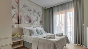 A modern bedroom with a large bed, a bedside table with a vase, and a wall with a floral painting. - Granaria B503 | 2 Balconies (Gdańsk)