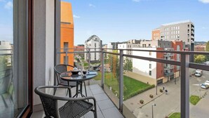 Un balcón con mesa y sillas, con vistas a un paisaje urbano de edificios y cielo despejado.
