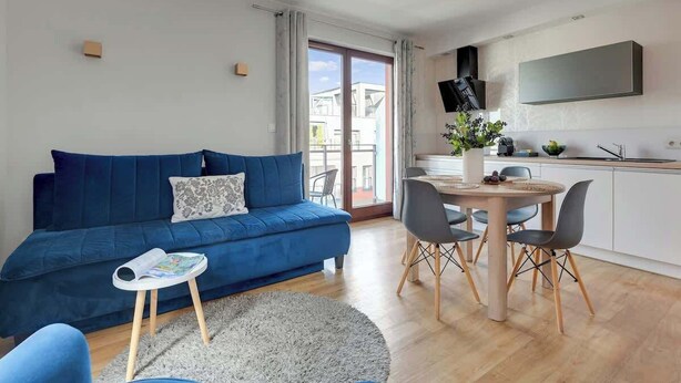 Una sala moderna con un sofá azul, una mesita redonda y una zona de comedor con sillas.
