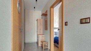 Un pasillo con un armario de madera, un pequeño estante de madera y una cama con una colcha azul en la habitación contigua.