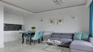 En moderne stue med en grå sofa, et glasbord og et spiseområde med en bordplade af sort marmor.