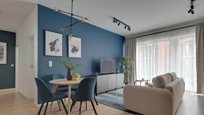 Moderni olohuone, jossa on sininen tehosteseinä, sohva, ruokapöytä tuoleineen, televisio ja suuri ikkuna, jossa on verhot.