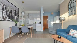 Ein modernes Wohnzimmer mit einem blauen Sofa, einer Essecke mit Stühlen, einer Küche im Hintergrund und einem großen Stadtbild an der Wand.