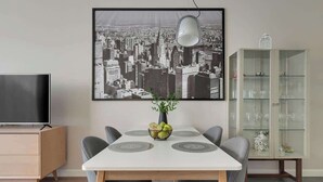 Ein Essbereich mit Stadtbild-Kunstwerk, einem Fernseher, einer Vitrine und einem Tisch mit Stühlen.
