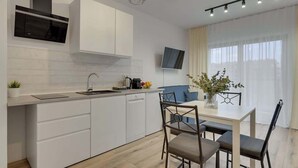 A modern kitchen with white cabinets, a built-in oven, and a dining area with a table and chairs. - Nadmotławie 81 | Riverside | Sauna & Gym (Gdańsk)