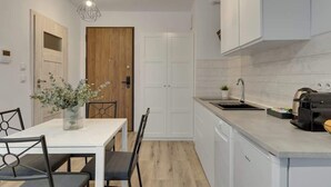 A modern kitchen with white cabinetry, a wooden door, a dining table with chairs, and a pendant light. - Nadmotławie 81 | Riverside | Sauna & Gym (Gdańsk)