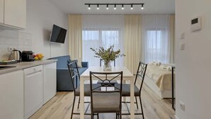 A modern kitchen with a dining area, a flat-screen TV, and a bed with a white bedspread. - Nadmotławie 81 | Riverside | Sauna & Gym (Gdańsk)