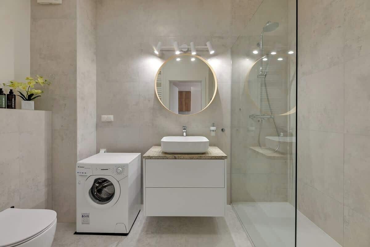 Un baño moderno con lavadora, un lavabo con espejo y ducha con mampara de cristal.