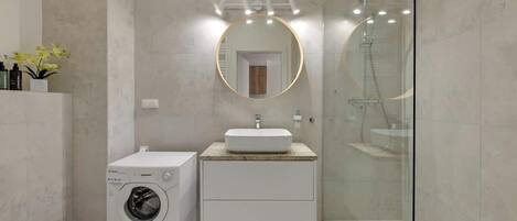 Un baño moderno con lavadora, un lavabo con espejo y ducha con mampara de cristal.