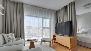 Une chambre d’hôtel moderne dotée d’une grande fenêtre, d’un téléviseur à écran plat, d’un canapé, d’un fauteuil, d’une petite table et d’un lit.