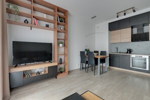 A modern living room with a flat-screen TV, wooden shelving, and a dining area with chairs and a table. - Letnica 2 with Terrace | Perfect Stay (Gdańsk)