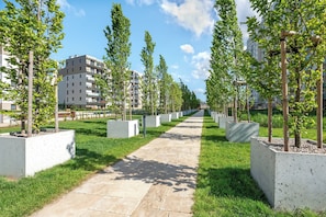 A pathway lined with trees and concrete planters, leading to a multi-story building. - Letnica 2 with Terrace | Perfect Stay (Gdańsk)