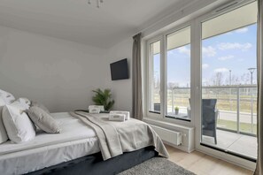 Ein modernes Schlafzimmer mit einem großen Bett, einem Flachbildfernseher, einer Topfpflanze und Blick ins Freie.
