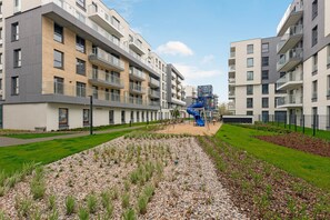 Ein modernes Apartmenthaus mit mehreren Balkonen, einem Spielplatz und einem angelegten Garten.