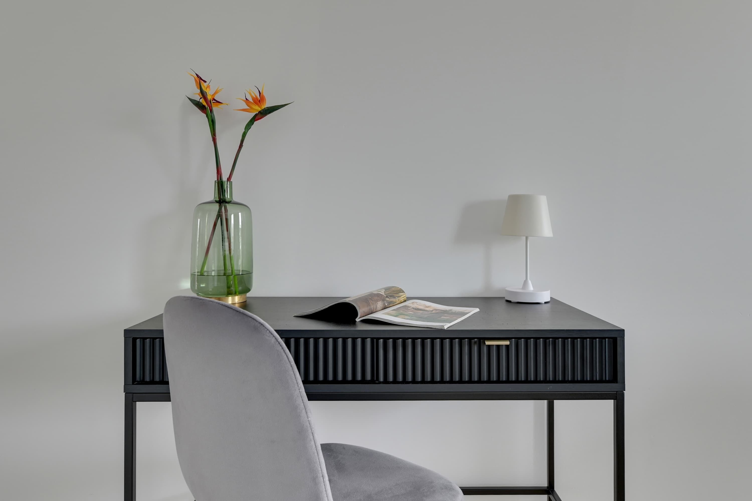 A modern desk with a lamp, a vase with flowers, and a magazine.