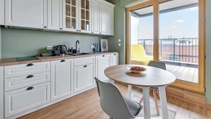 Une cuisine moderne avec des meubles blancs, une table de salle à manger ronde et un balcon agrémenté d’une chaise jaune.
