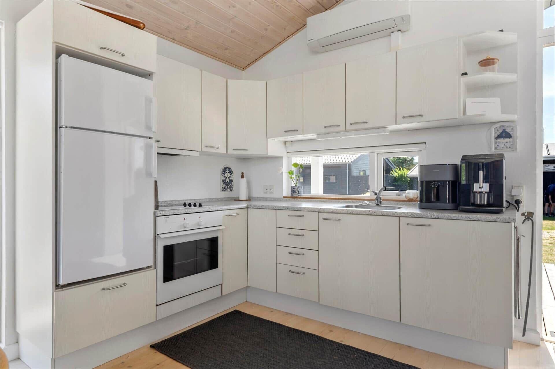 A modern kitchen with white cabinetry, a built-in oven, a refrigerator, and a coffee maker.