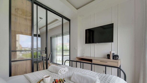 A hotel room with a bed, a TV, a desk, and a view through a glass door.