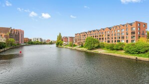 A river with buildings on both sides, including a red brick building with multiple windows and a modern building with a flat roof.