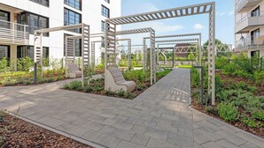 Et moderne udendørsområde med belagt sti, siddepladser og beplantning.