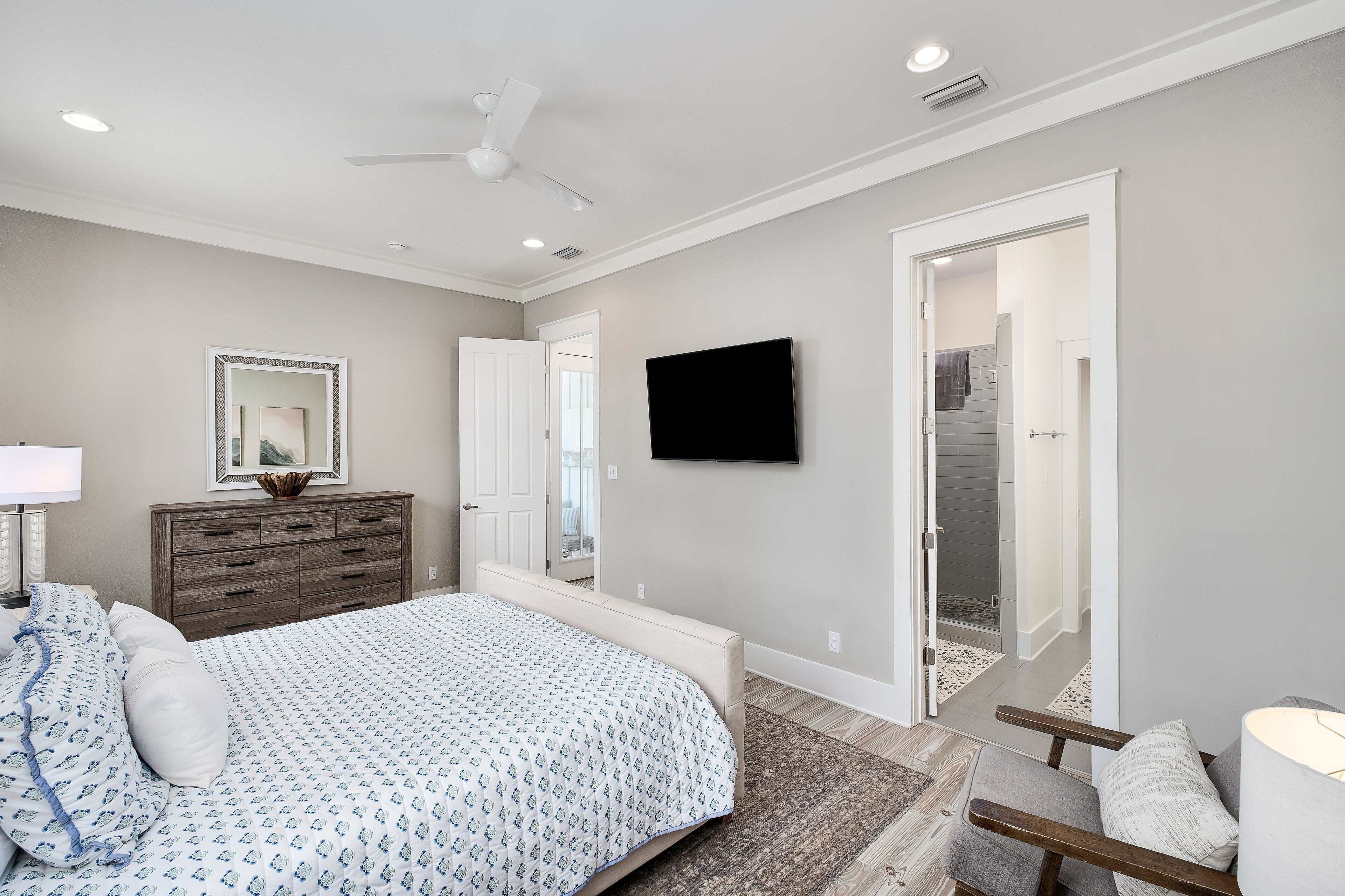 A bedroom with a bed, dresser, TV, and a door leading to a bathroom.