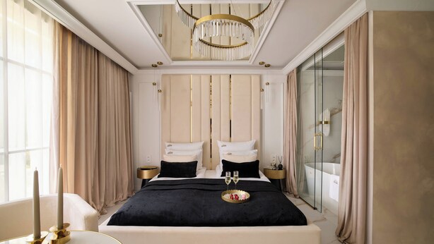 A luxurious bedroom with a large bed, a chandelier, a glass shower, and a round table with candles. - Portovo 193 | Jacuzzi Suite | Perfect for Couples (Gdańsk)
