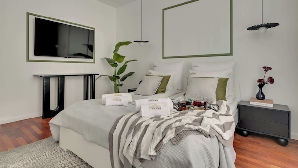 Ein modernes Schlafzimmer mit Bett, Nachttischen, einem Fernseher und einer Pflanze.