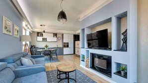 A modern living room with a sofa, a round coffee table, a fireplace, and a TV mounted on the wall. - Aura 222 | River View (Gdańsk)
