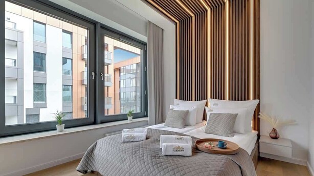 Une chambre d’hôtel moderne dotée d’une grande fenêtre, d’un lit recouvert d’une courtepointe matelassée, d’une table de chevet avec un plateau et d’un panneau décoratif mural.