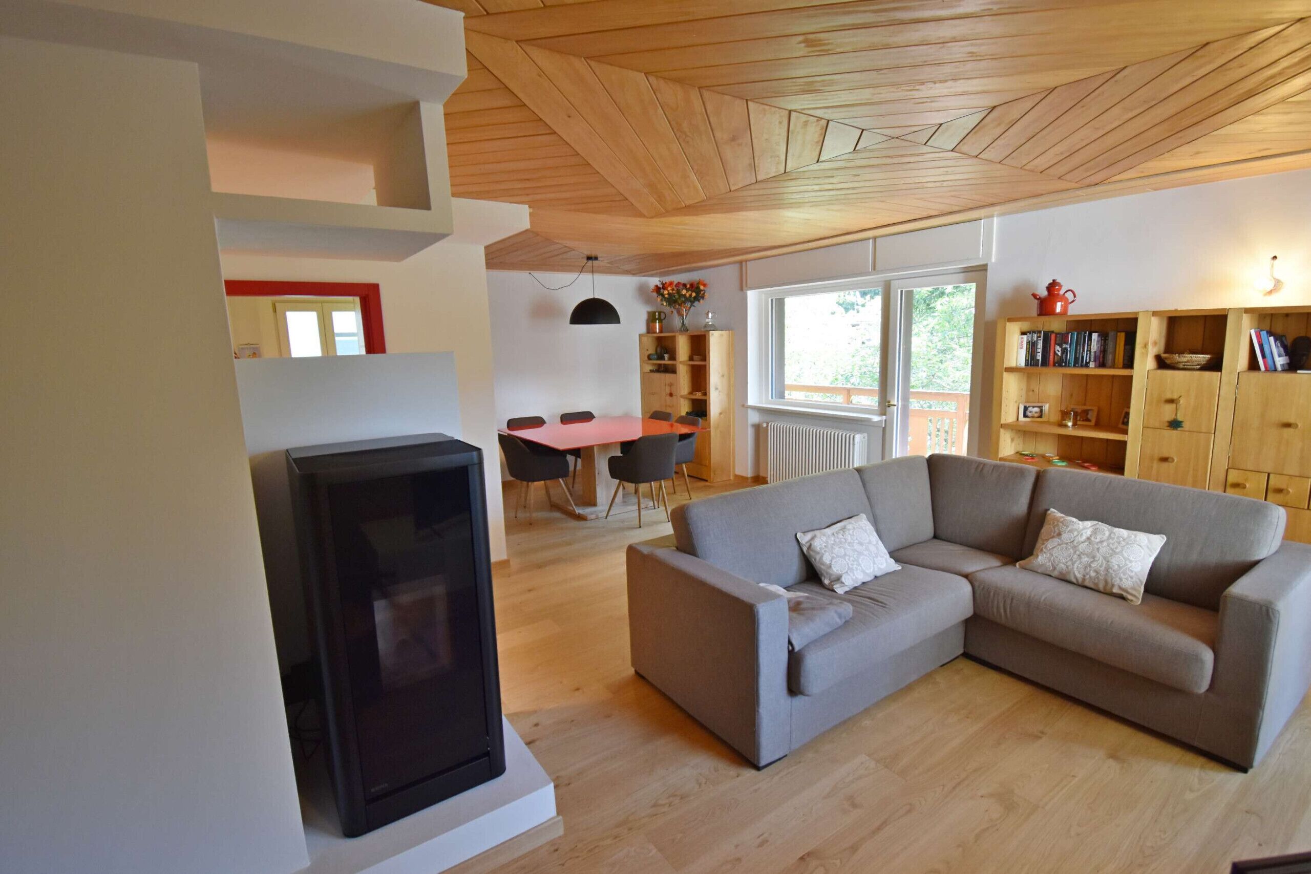 A modern living room with a sectional sofa, a flat-screen TV, a dining area with a table and chairs, and a bookshelf.