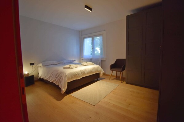A bedroom with a bed, a chair, a window, and a wardrobe. - CROZZON view Apartment MhD (Madonna di Campiglio)
