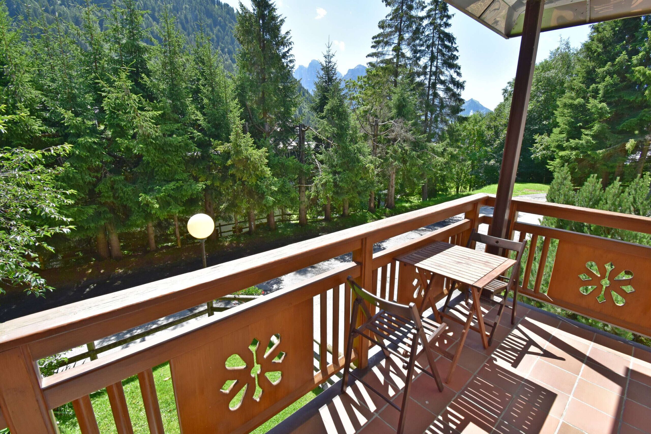 A balcony with a table and chairs, overlooking a forested area with mountains in the background.