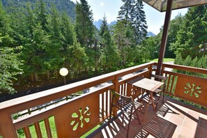 A balcony with a table and chairs, overlooking a forested area with mountains in the background. - CROZZON view Apartment MhD (Madonna di Campiglio)