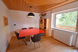 A room with a wooden ceiling, a red table with chairs, a bookshelf, and a window with a view of trees. - CROZZON view Apartment MhD (Madonna di Campiglio)